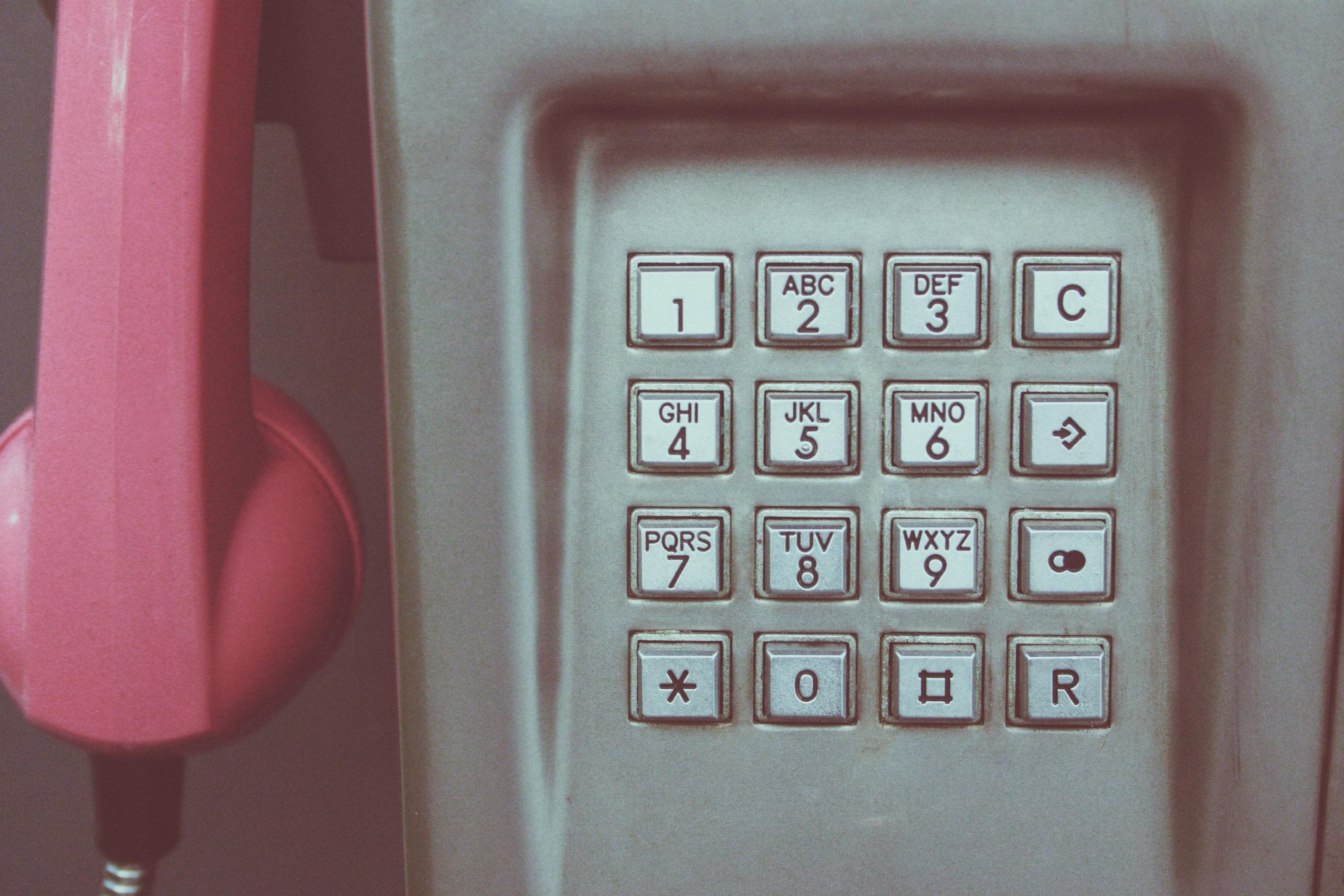 Close-up of a vintage payphone keypad with pink receiver, highlighting retro technology.